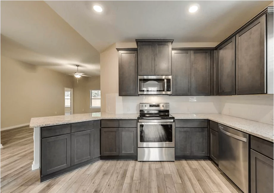 Empty model home kitchen featuring grey flooring, a silver stove and microwave, and dark cabinetry for a sleek, modern contrast. The clean lines and neutral tones highlight the updated, functional layout.