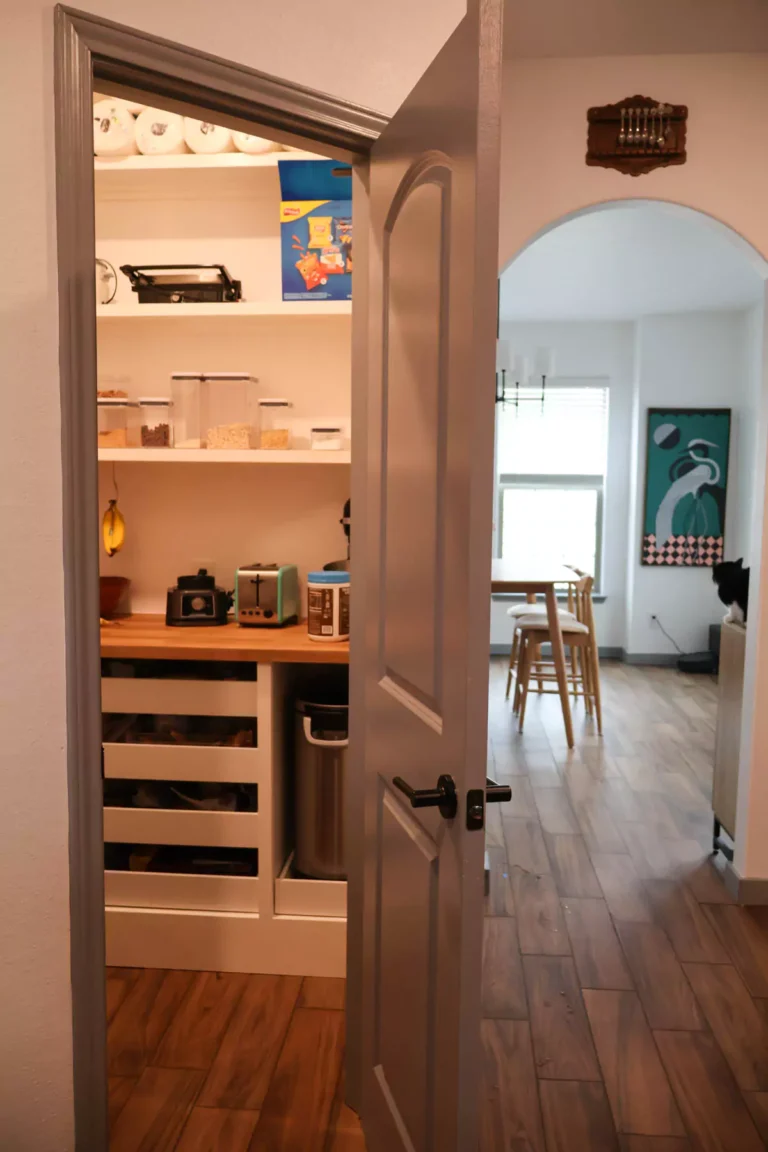 Custom pantry shelves with built-in kick board, organized with labeled baskets, glass jars, and canned goods. The wooden shelving offers both function and style, maximizing vertical storage in a clean, efficient layout.