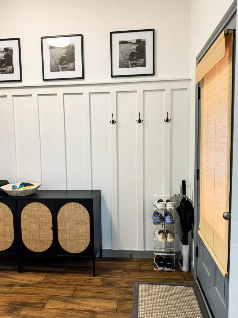 White board and batten wall installed at two-thirds height, topped with a row of black picture frames on the upper wall. The board and batten section features sleek black hardware, adding contrast and a modern touch to the classic wall treatment.